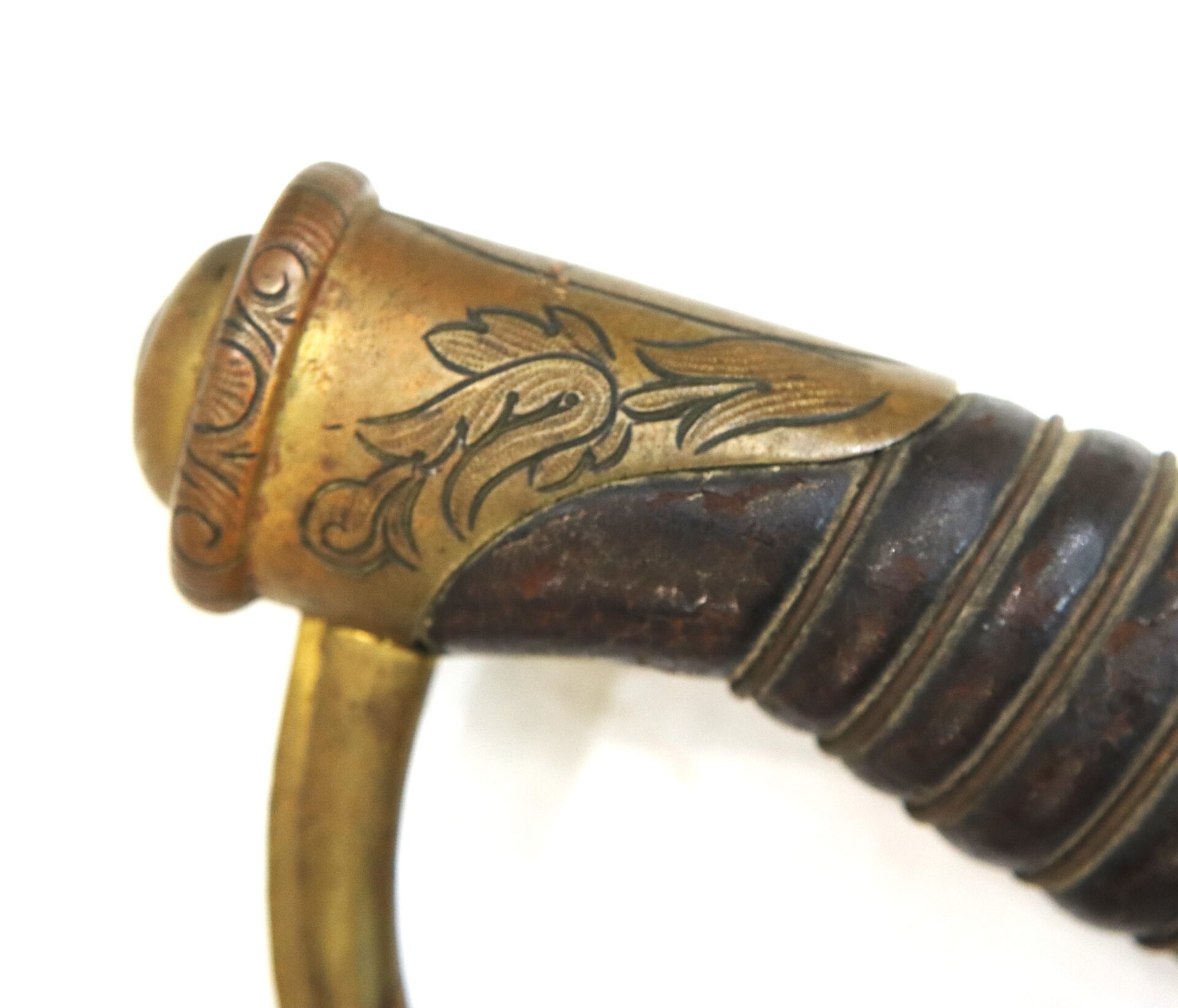 Close-up of a sword hilt with a brass pommel and guard, featuring engraved decorative patterns and a wrapped grip.