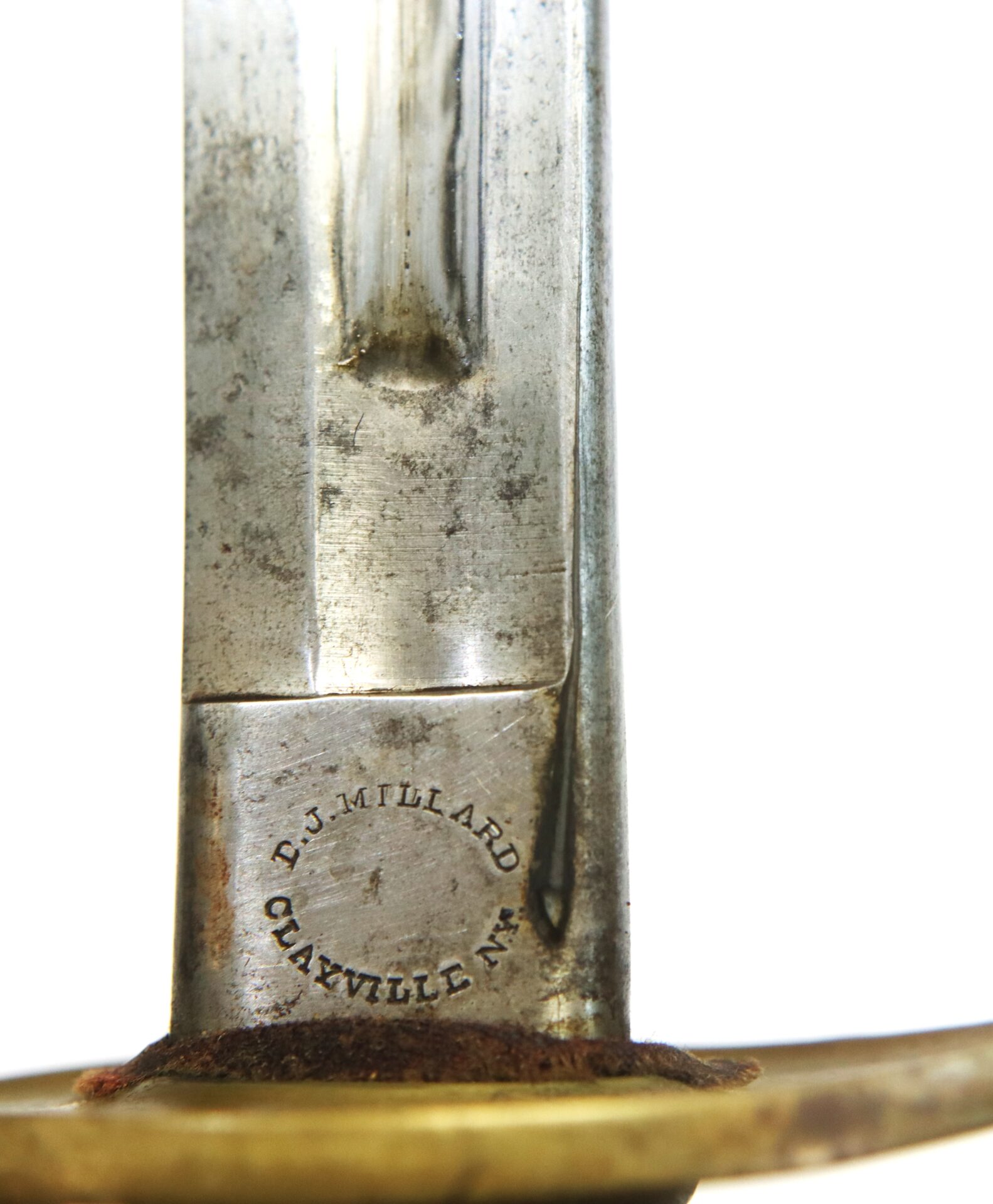 Close-up of a metal sword blade with the inscription "E.J. Millard Clayville N.Y." near the hilt, alongside a brass component.