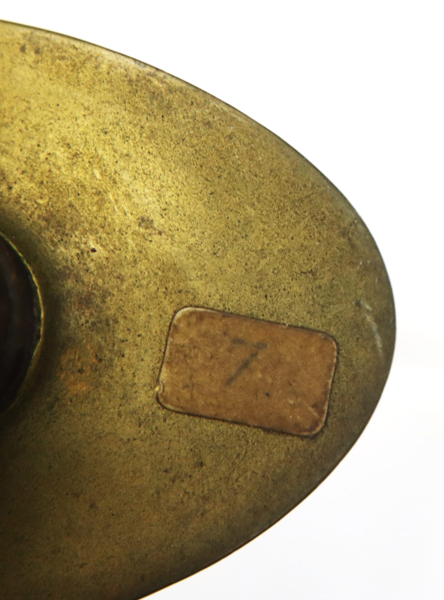 Close-up of a worn brass object with a small rectangular label displaying the number 7.