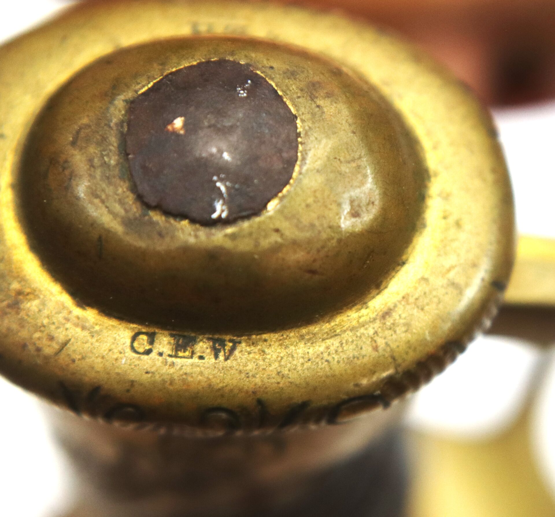 Close-up of a brass object with a central dark circular area and the letters "C.L.W." engraved on the metal surface.