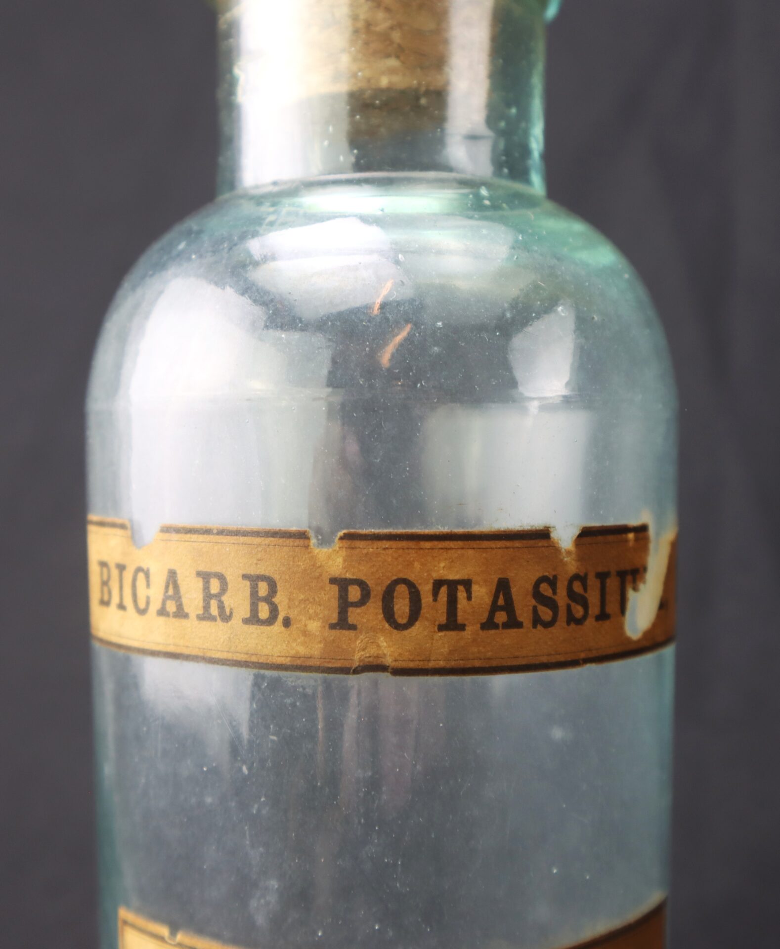 Clear glass bottle with a cork stopper and a brown label reading "BICARB. POTASS." The label shows signs of wear and age.