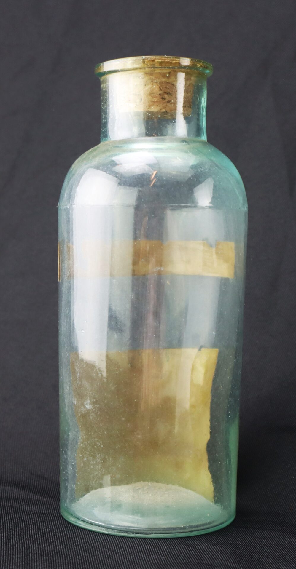 Clear glass apothecary jar with a wide neck and brass or metal rim, displayed against a dark, plain background.