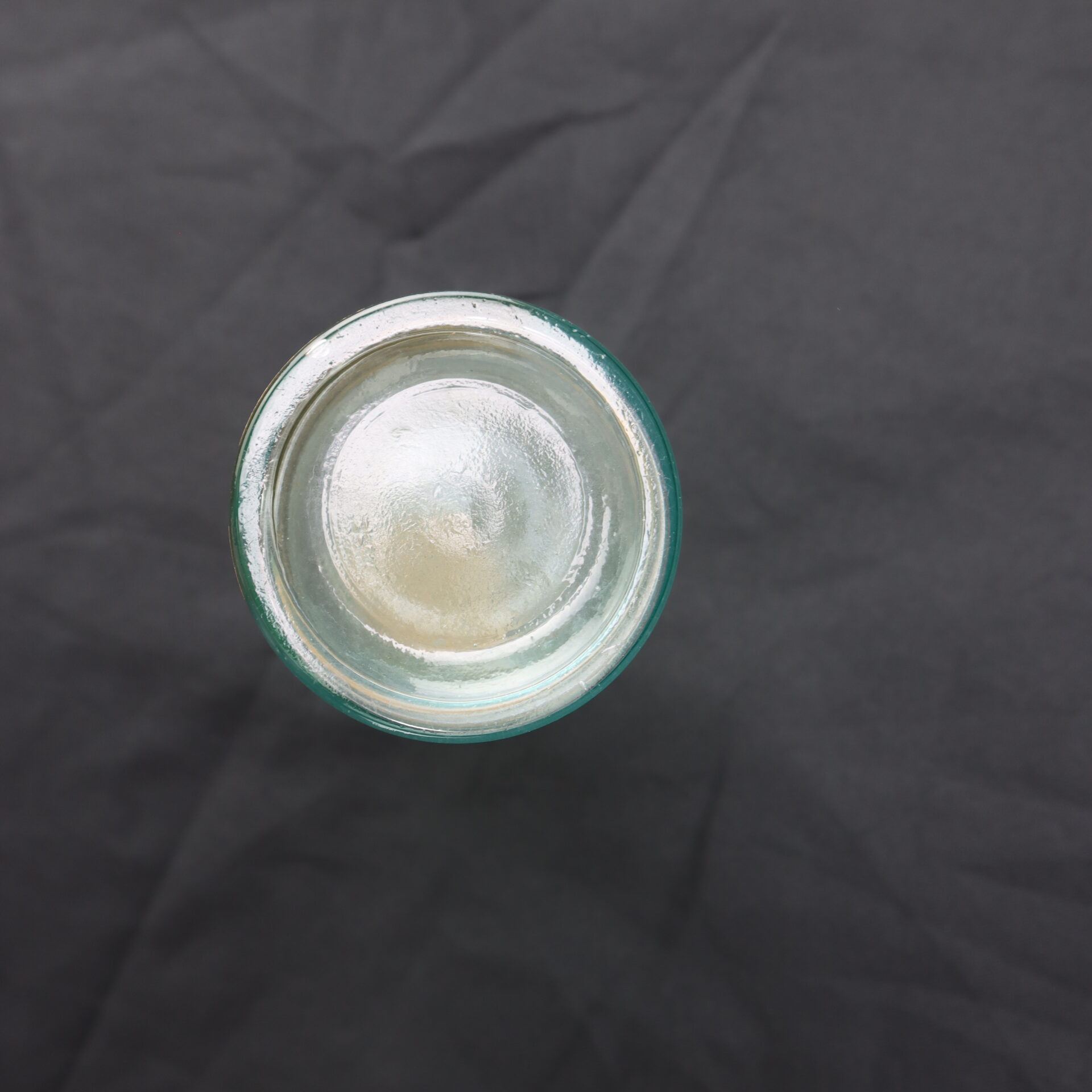 A clear glass jar viewed from above, placed on a dark, slightly wrinkled surface.