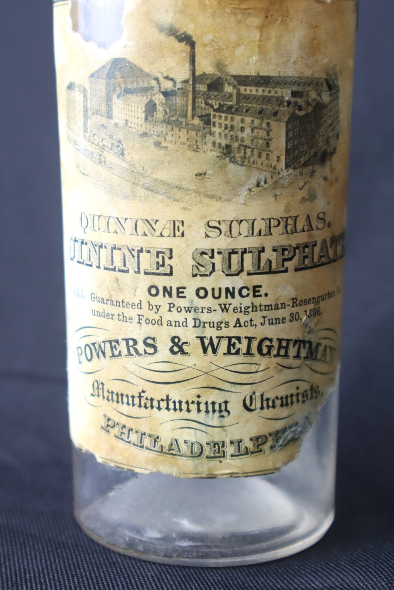 A vintage glass bottle labeled "Quinine Sulphate, One Ounce," manufactured by Powers & Weightman, Philadelphia, with an old factory illustration and aged paper label.
