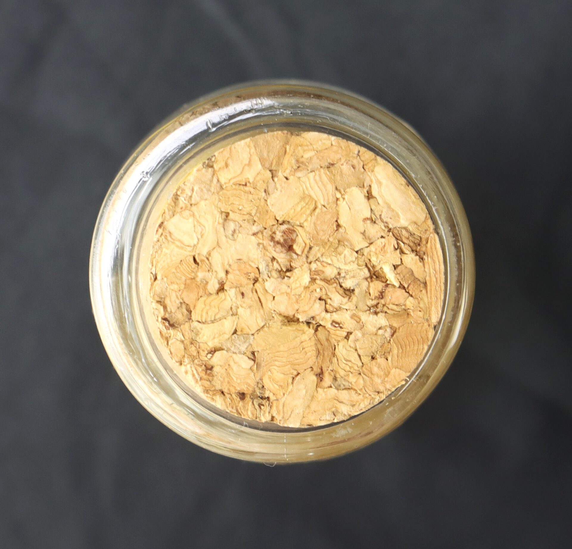 A glass jar filled with dried ginger slices, viewed from above against a dark background.