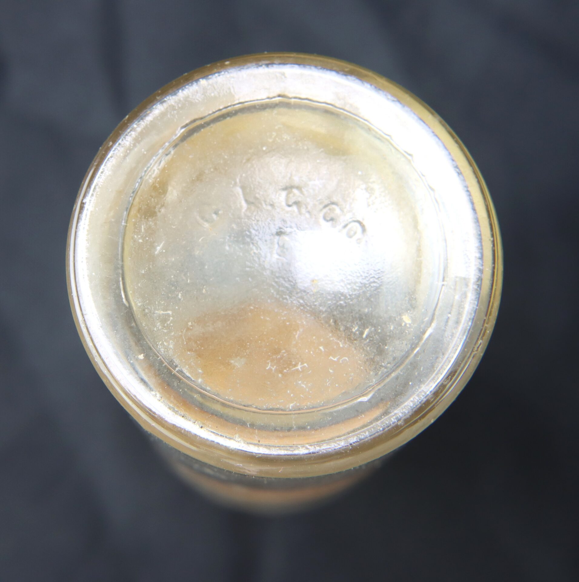 A close-up view of the bottom of a clear glass jar with faintly embossed numbers on its base, set against a dark background.