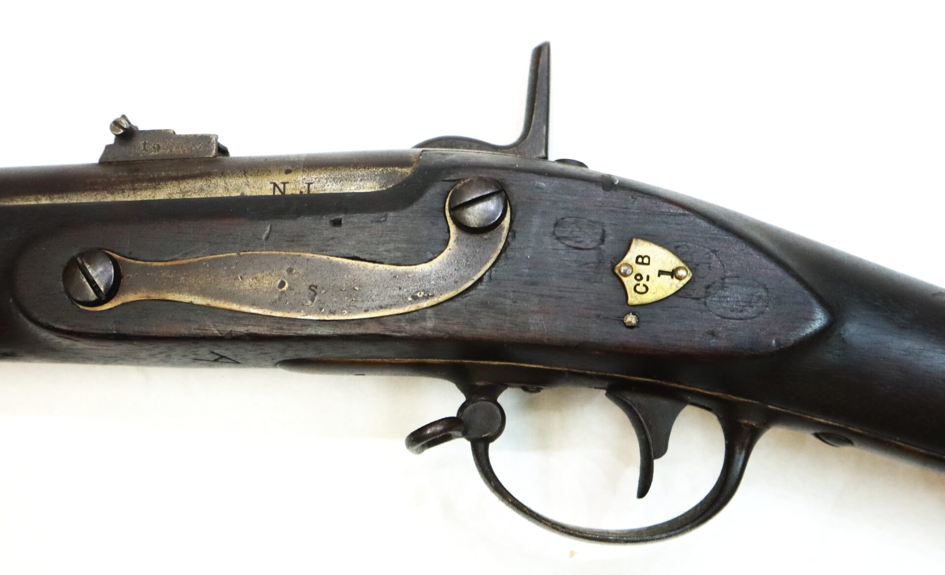 Close-up of the lock mechanism and trigger area of an antique percussion rifle with metal and brass components on a dark wooden stock.
