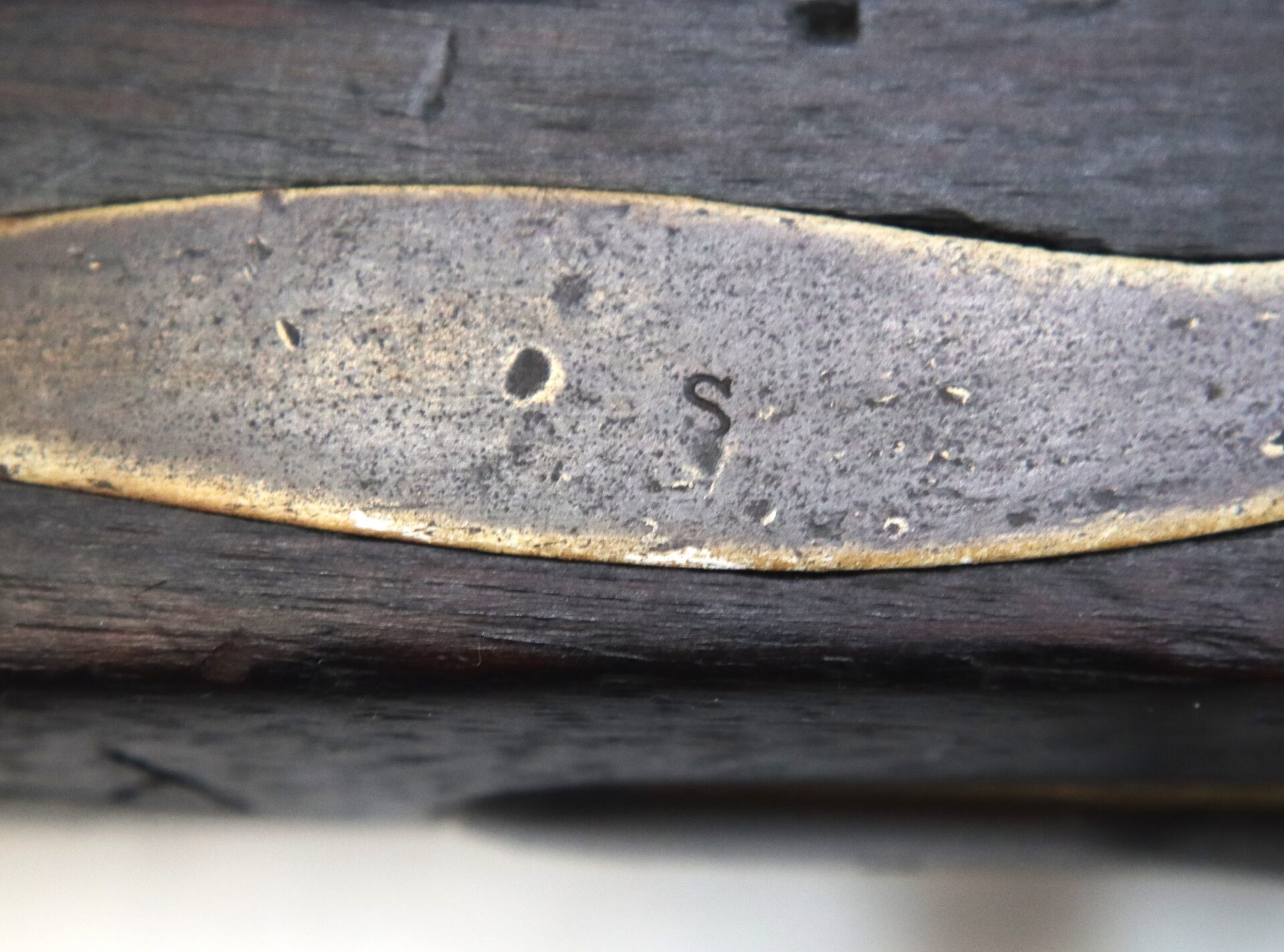 Close-up of a metal plate with the letters "O S" engraved on a dark wooden surface.