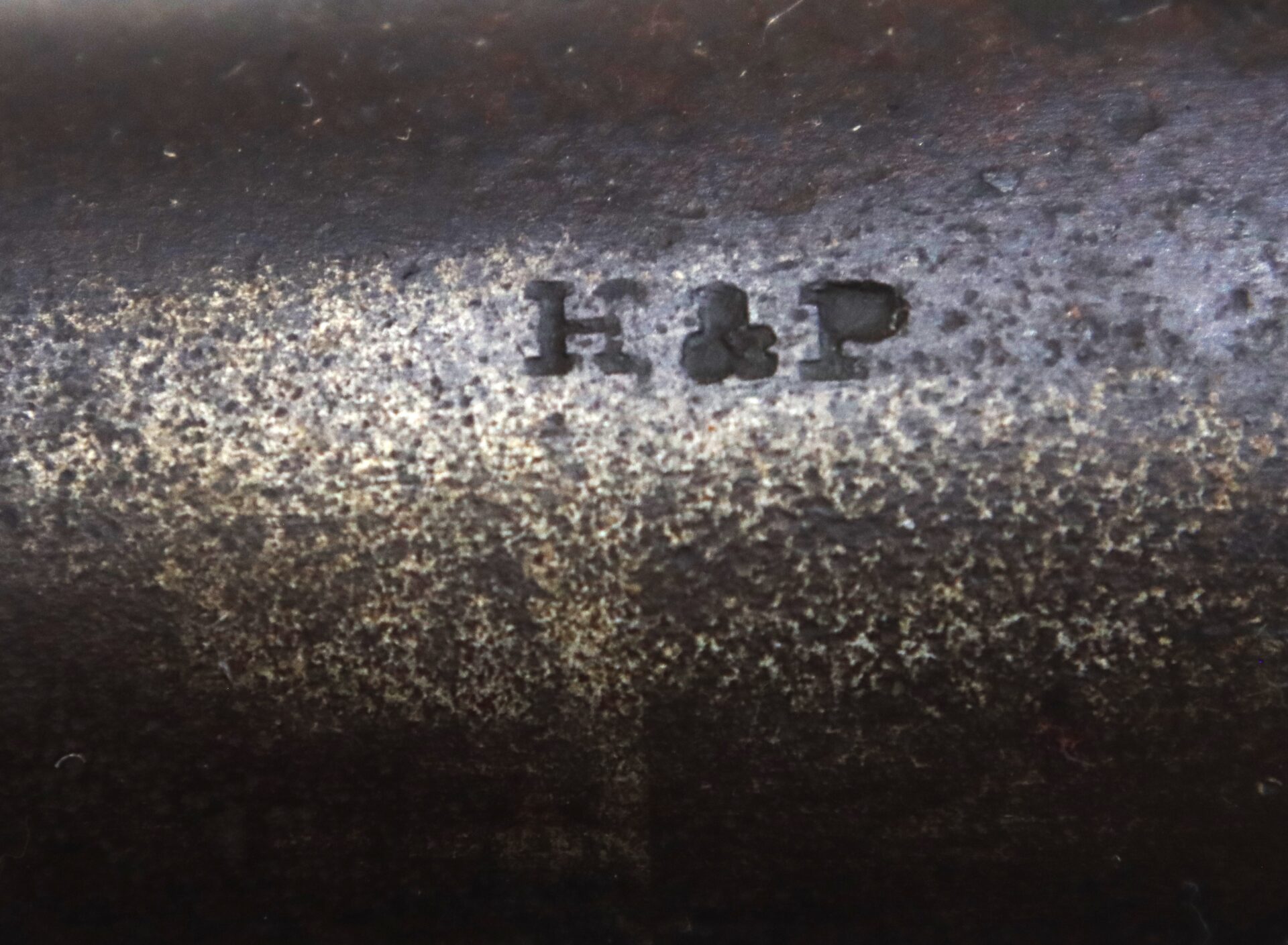 Close-up of a metal surface with the engraved letters "H & P" visible among areas of rust and texture.