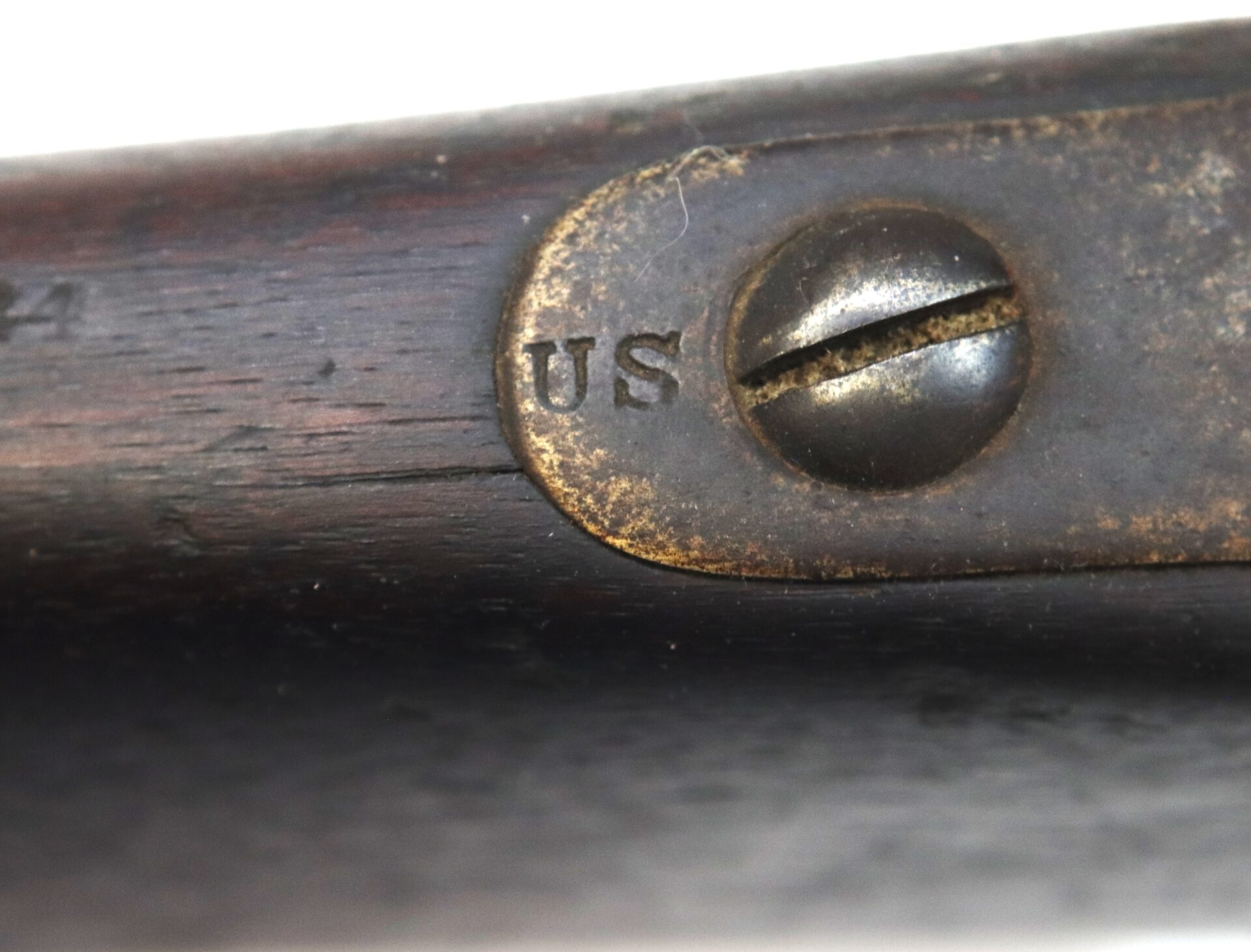 Close-up of an old wooden object with a metal plate featuring a screw and engraved letters "US.
