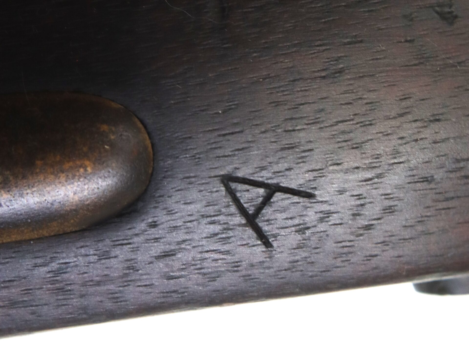 Close-up of a dark wooden surface featuring a carved letter "A" near a rounded metal piece.