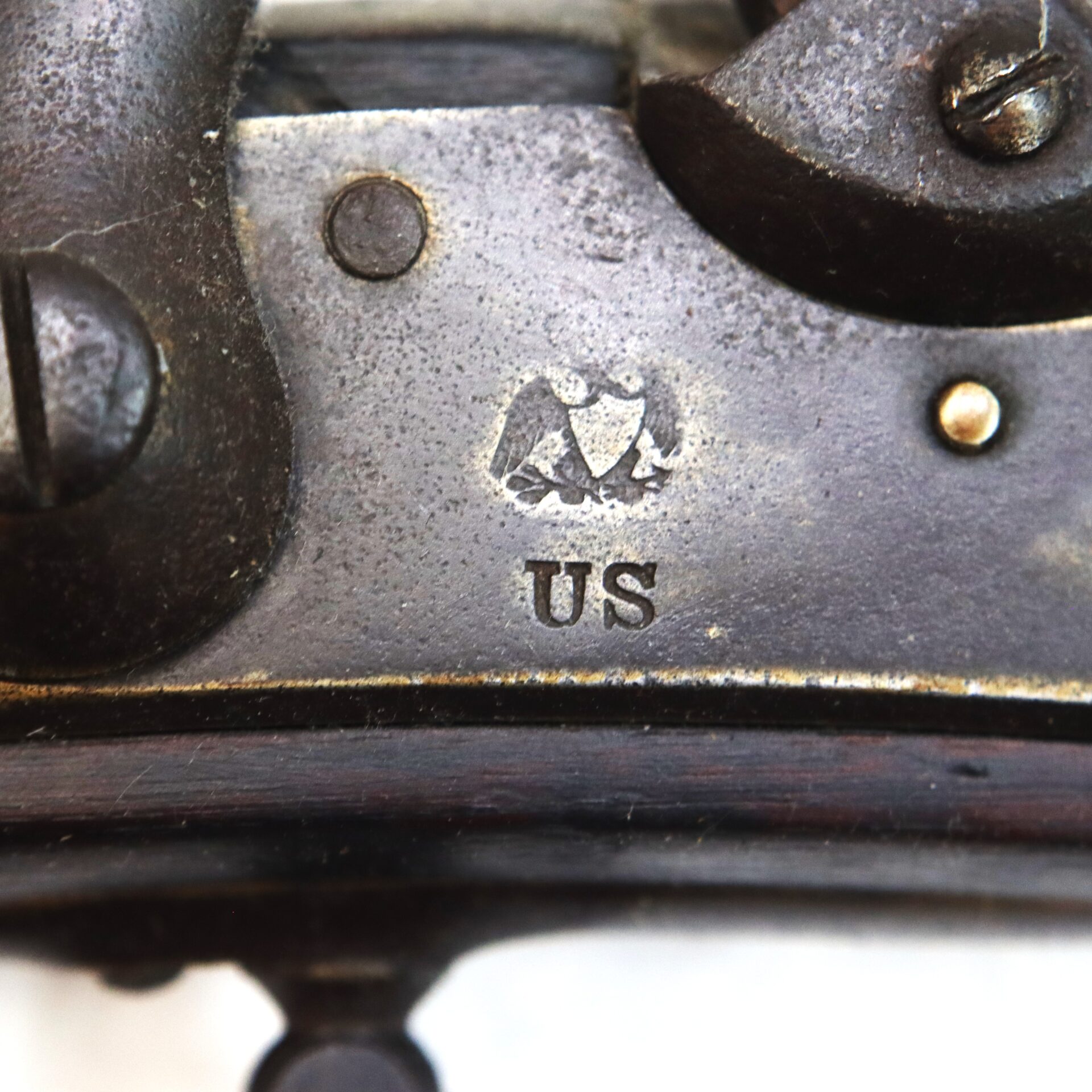 Close-up of a metal surface stamped with an eagle symbol above the letters "US," part of an antique firearm mechanism.