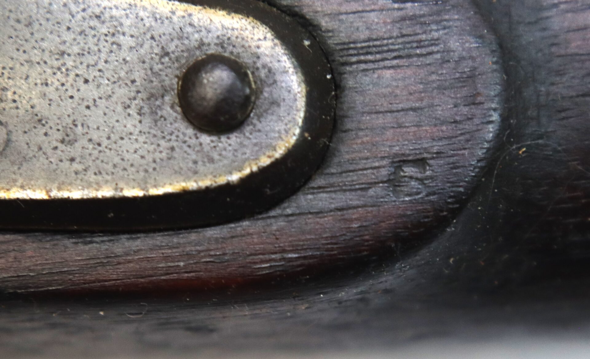 Close-up of a metal plate with a screw on a wooden surface, showing a stamped number "5" on the wood near the metal edge.