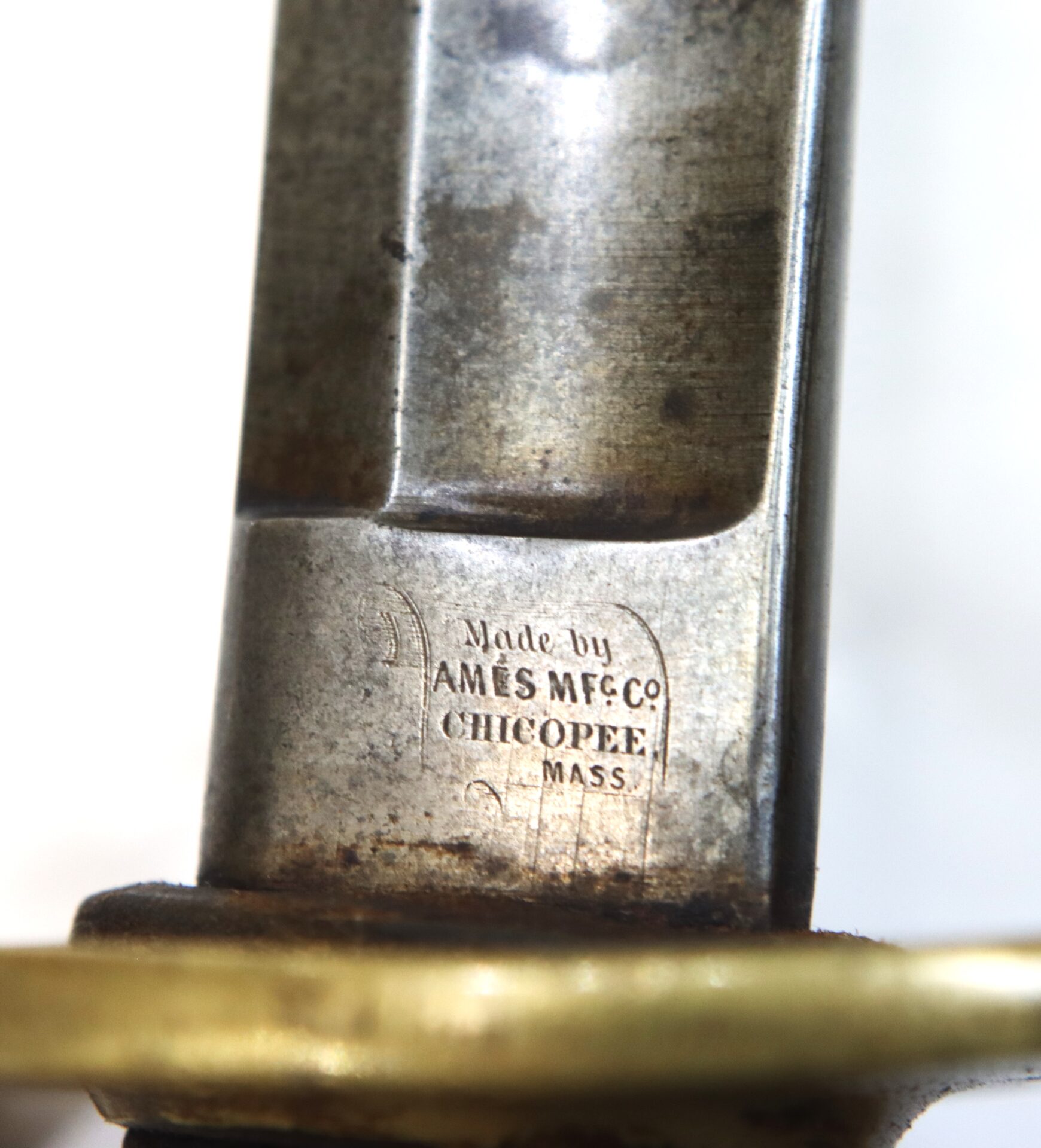 Close-up of a metal blade engraved with "Made by AMES MFG. CO. CHICOPEE, MASS." above a brass guard.