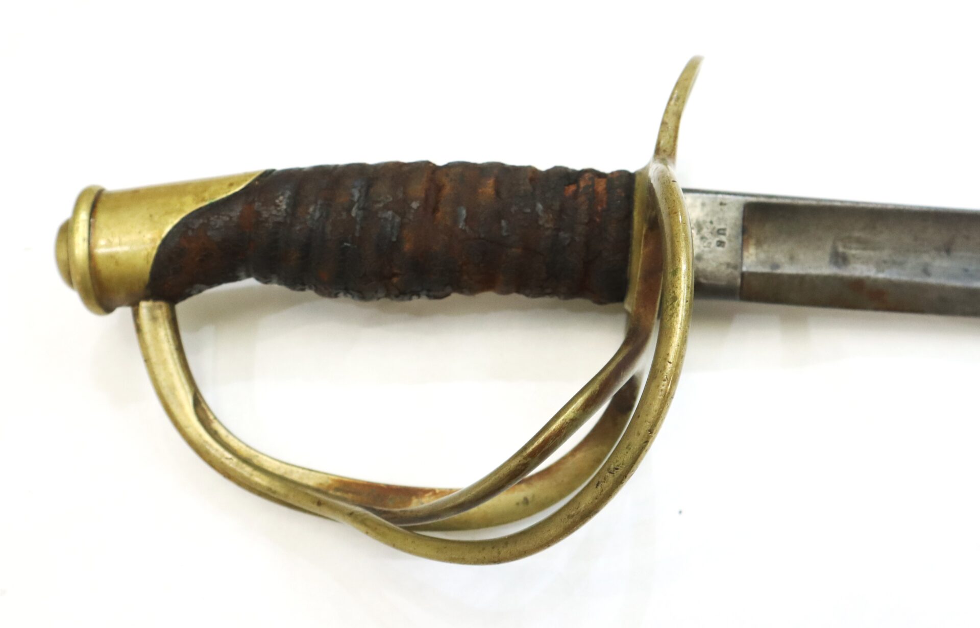 Close-up of the handle and guard of an antique sword with a brass hilt and a weathered, wrapped grip against a white background.