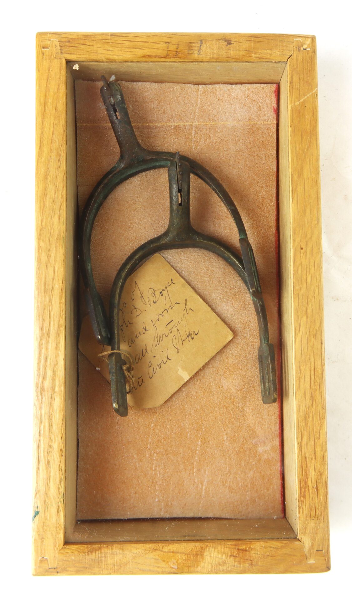 A single antique metal spur displayed in a wooden box, accompanied by a handwritten note on a piece of paper beneath it.