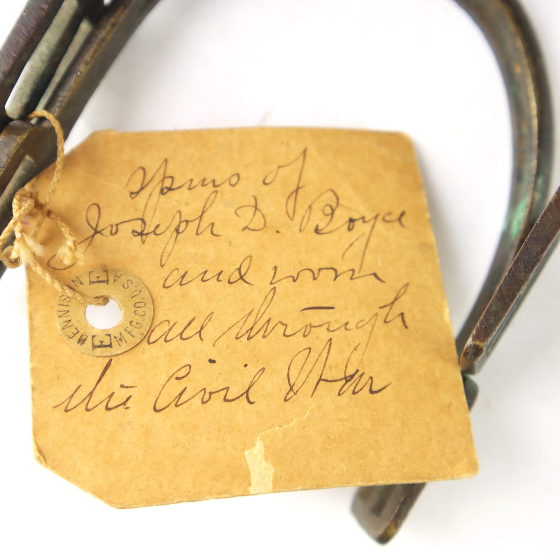 A handwritten tag attached to a metal object reads: "Memo of Joseph D. Boyce and worn all through the Civil War".