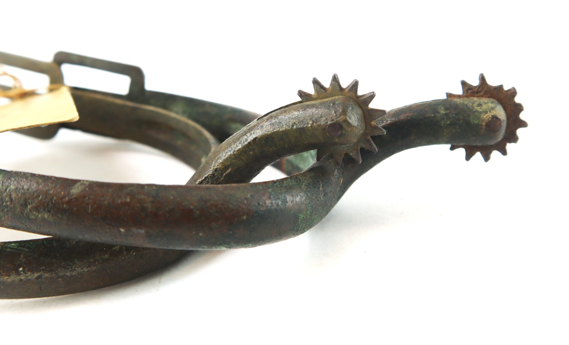 Close-up of a rusted metal spur with a rowel, showing signs of wear and aging, on a plain white background.