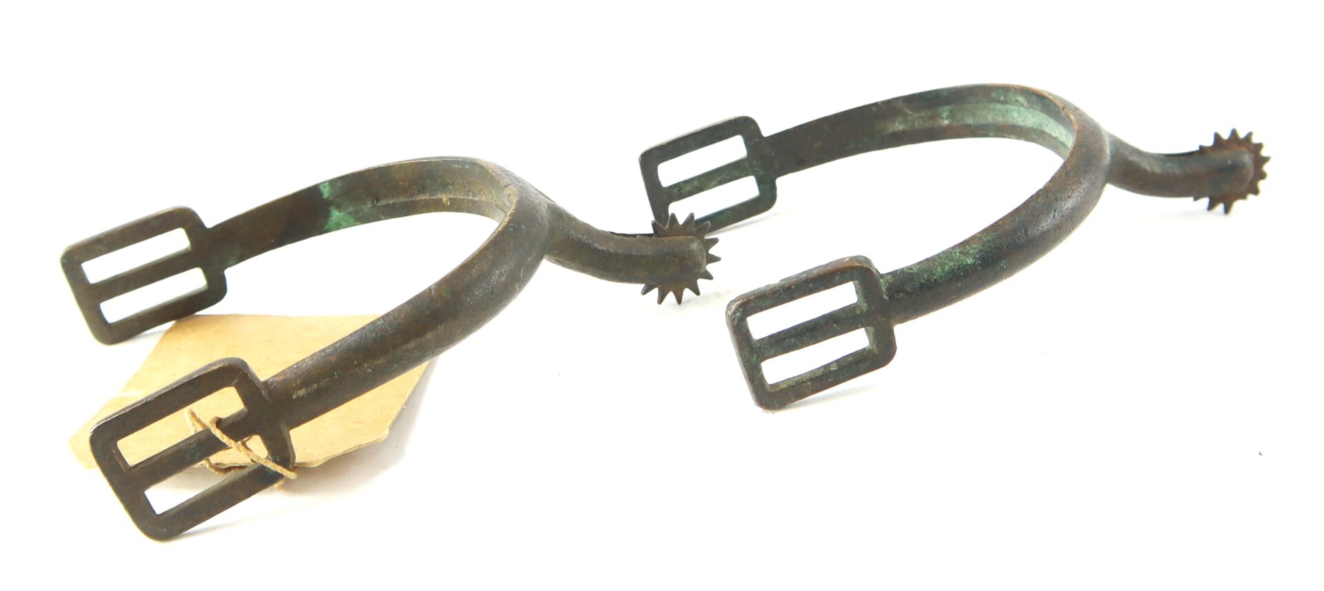 A pair of antique metal spurs with rowel wheels and rectangular buckle slots, shown against a white background.