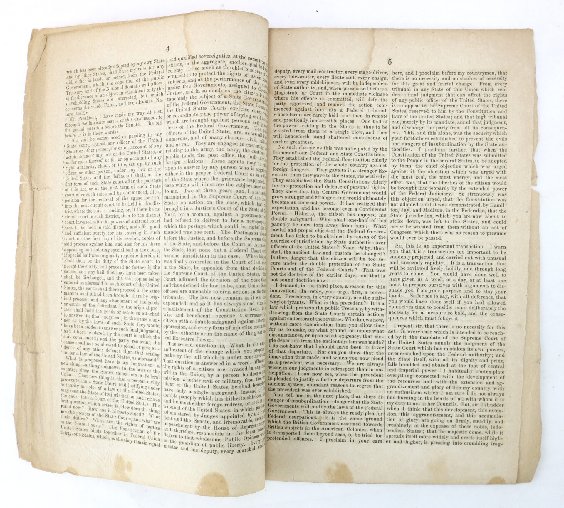 An old, yellowed book lies open, displaying densely packed text in three columns on each page, with frayed edges and visible stains at the bottom.