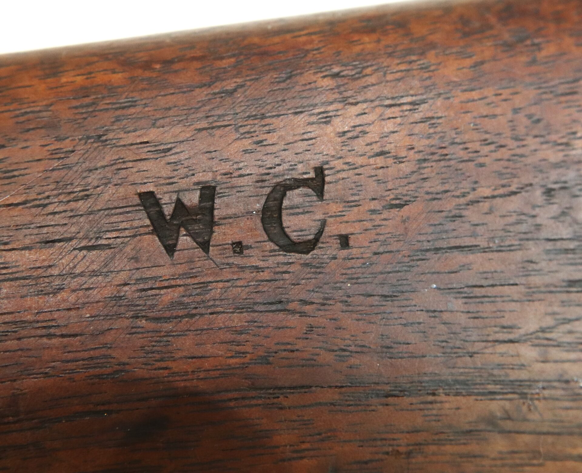 Close-up of wooden surface with the initials "W. C." engraved or stamped into it.