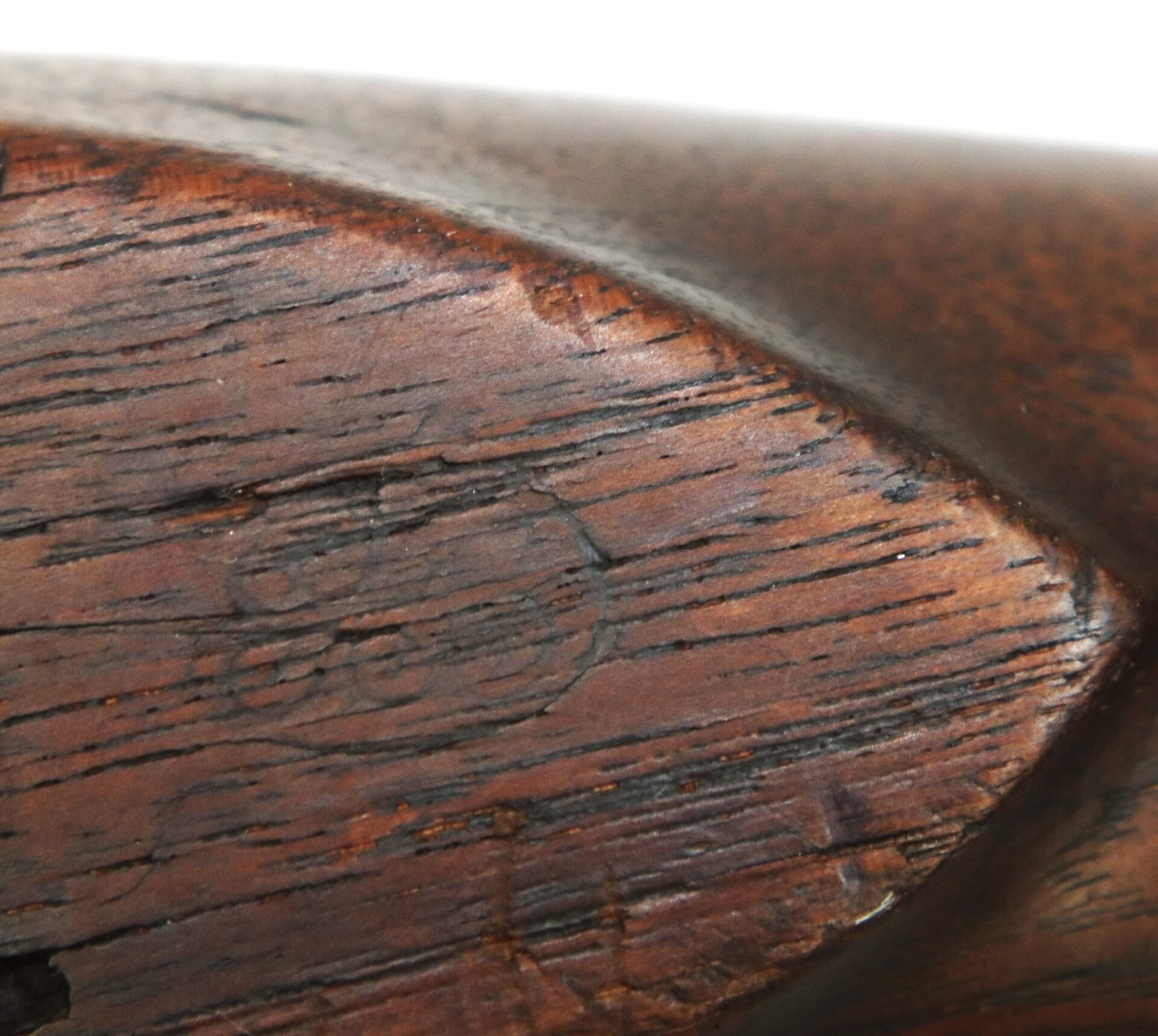 Close-up of a dark wooden surface with visible grain, scratches, and a faint circular stamp or marking in the center.