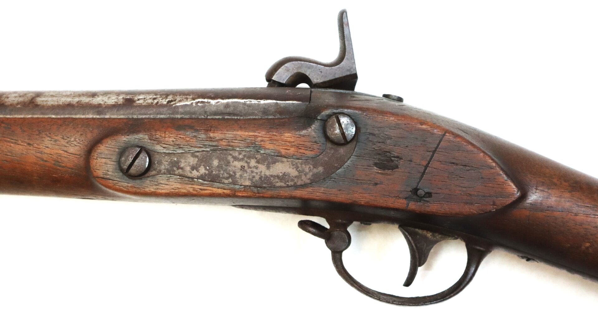 Close-up of the lock mechanism and trigger of an old, weathered flintlock or percussion rifle with a wooden stock on a white background.