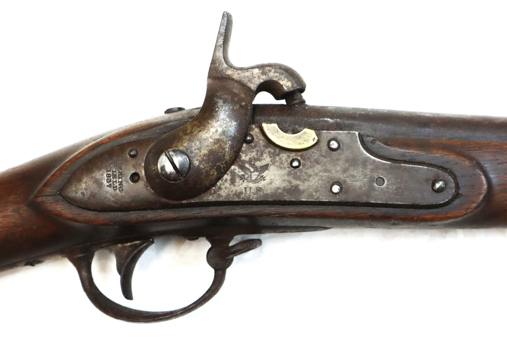 Close-up of an antique percussion lock musket, showing the hammer, trigger, and engraved metal plate on a wooden stock.