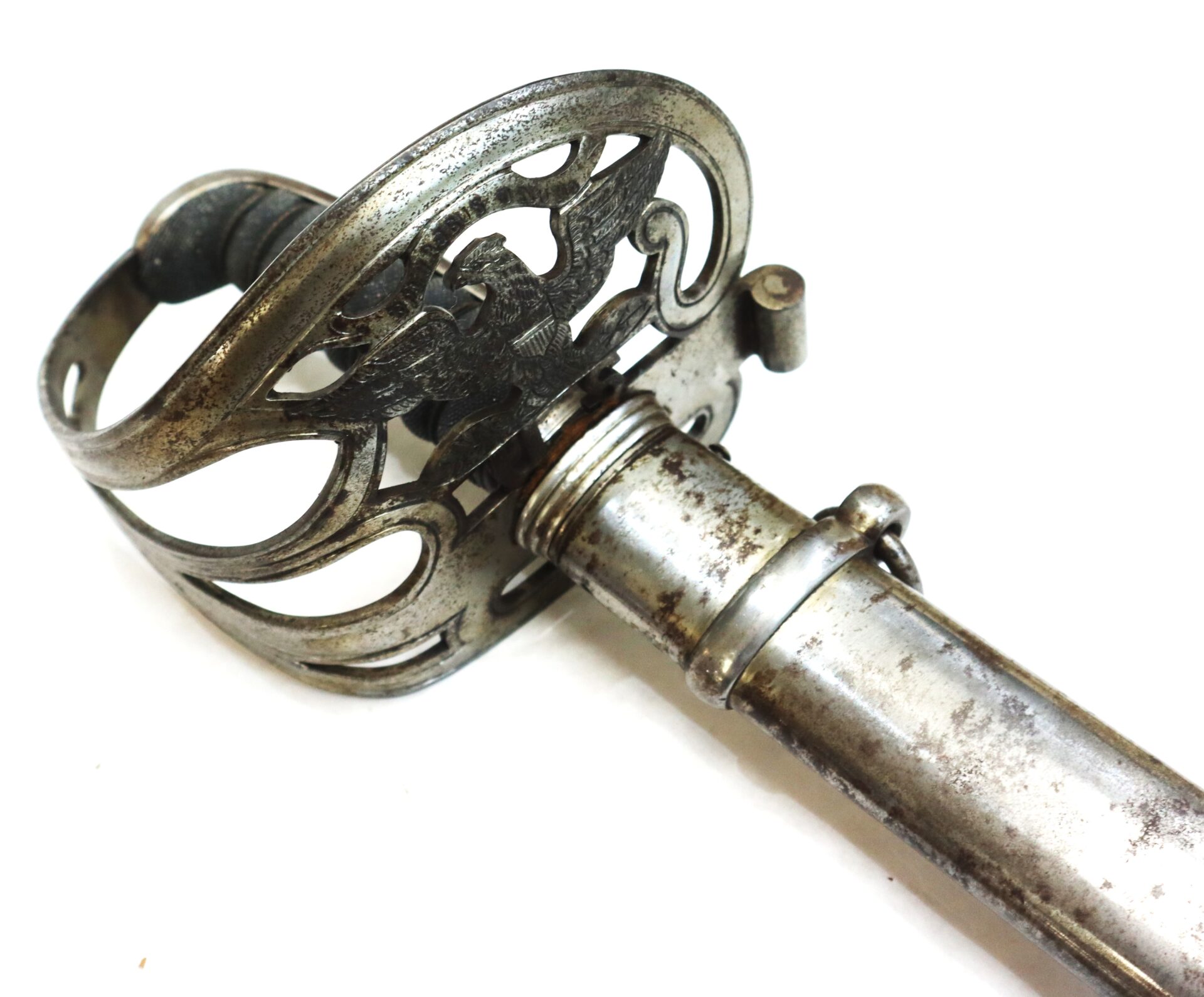 Close-up of the ornate hilt and guard of a vintage metal sword with some tarnish and wear, resting on a white background.