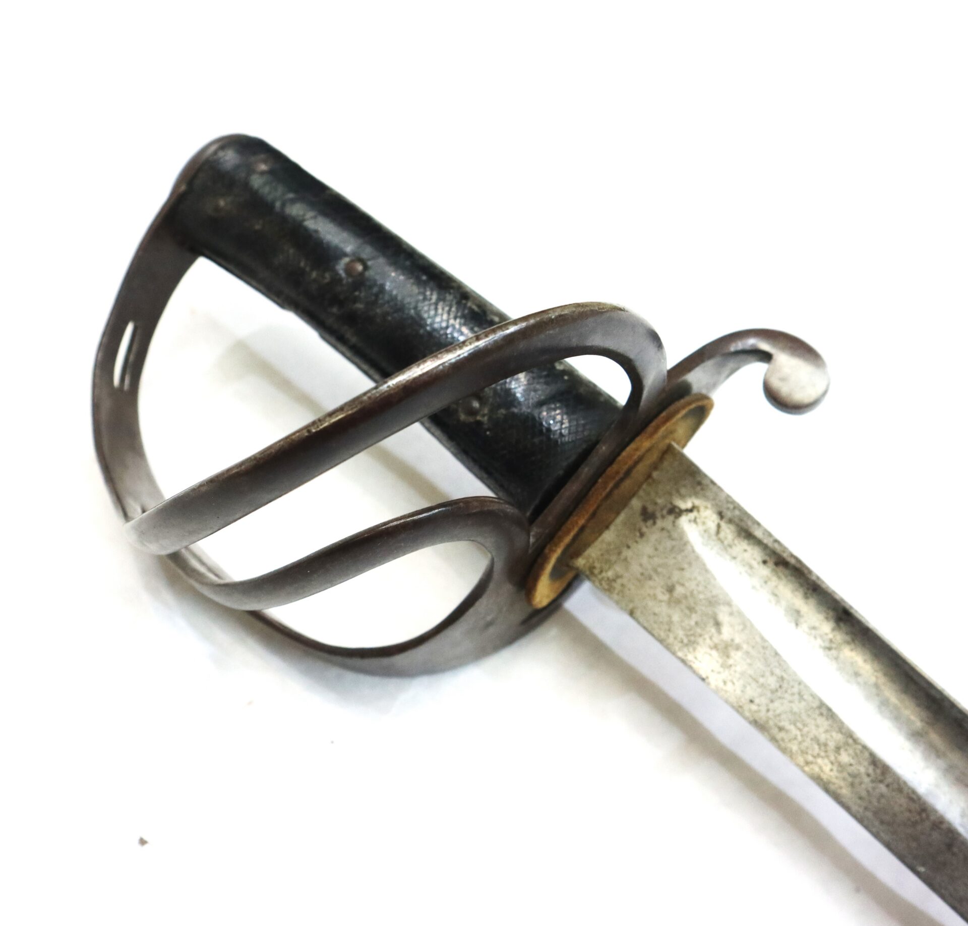 Close-up of a vintage sword with a metal guard, black textured handle, and a slightly tarnished blade, photographed on a white background.
