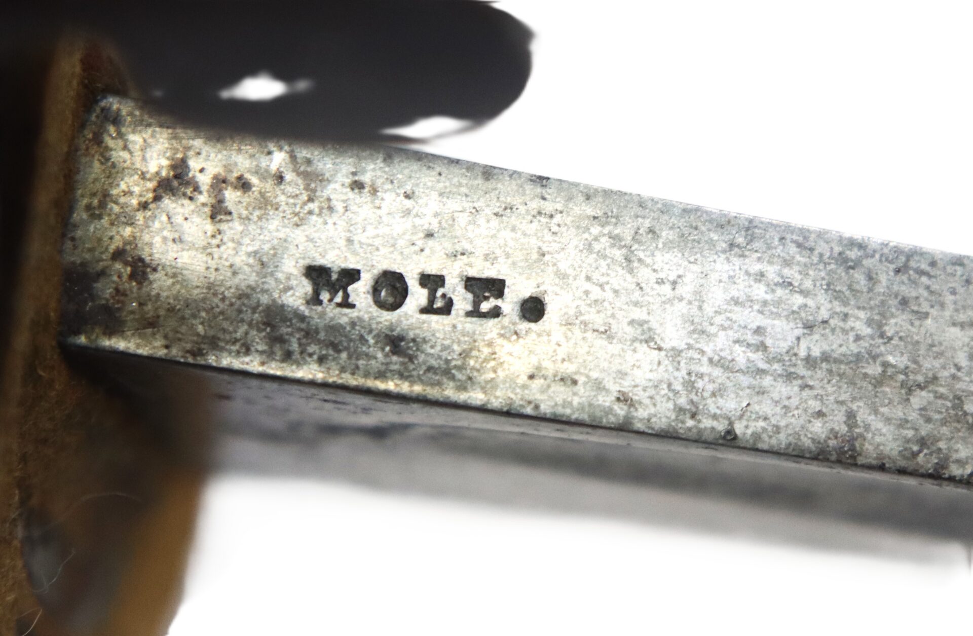 Close-up of a metal object with the word "MOLE." stamped into its surface. The metal appears slightly tarnished and worn.