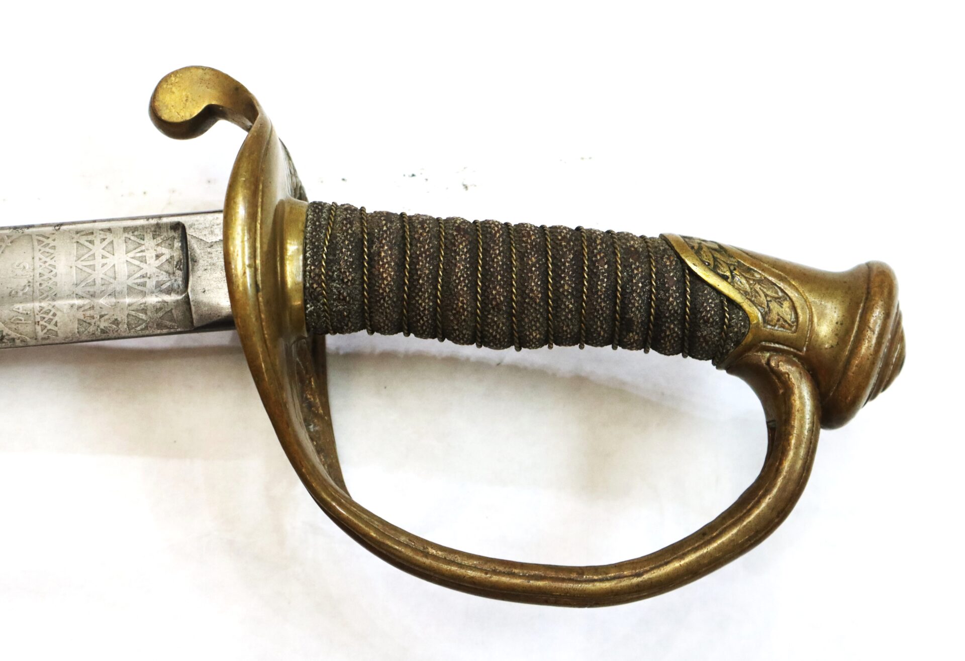 Close-up of a vintage sword hilt with a brass guard and wire-wrapped handle, partially showing the engraved blade on a white background.