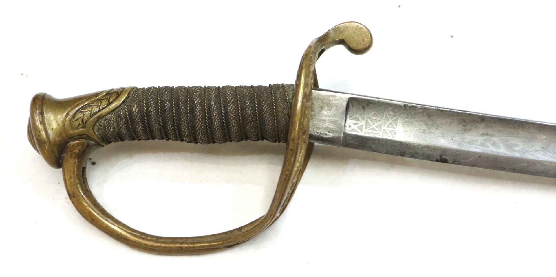 Close-up of a sword hilt with a brass guard, textured grip, and a partially etched steel blade on a white background.
