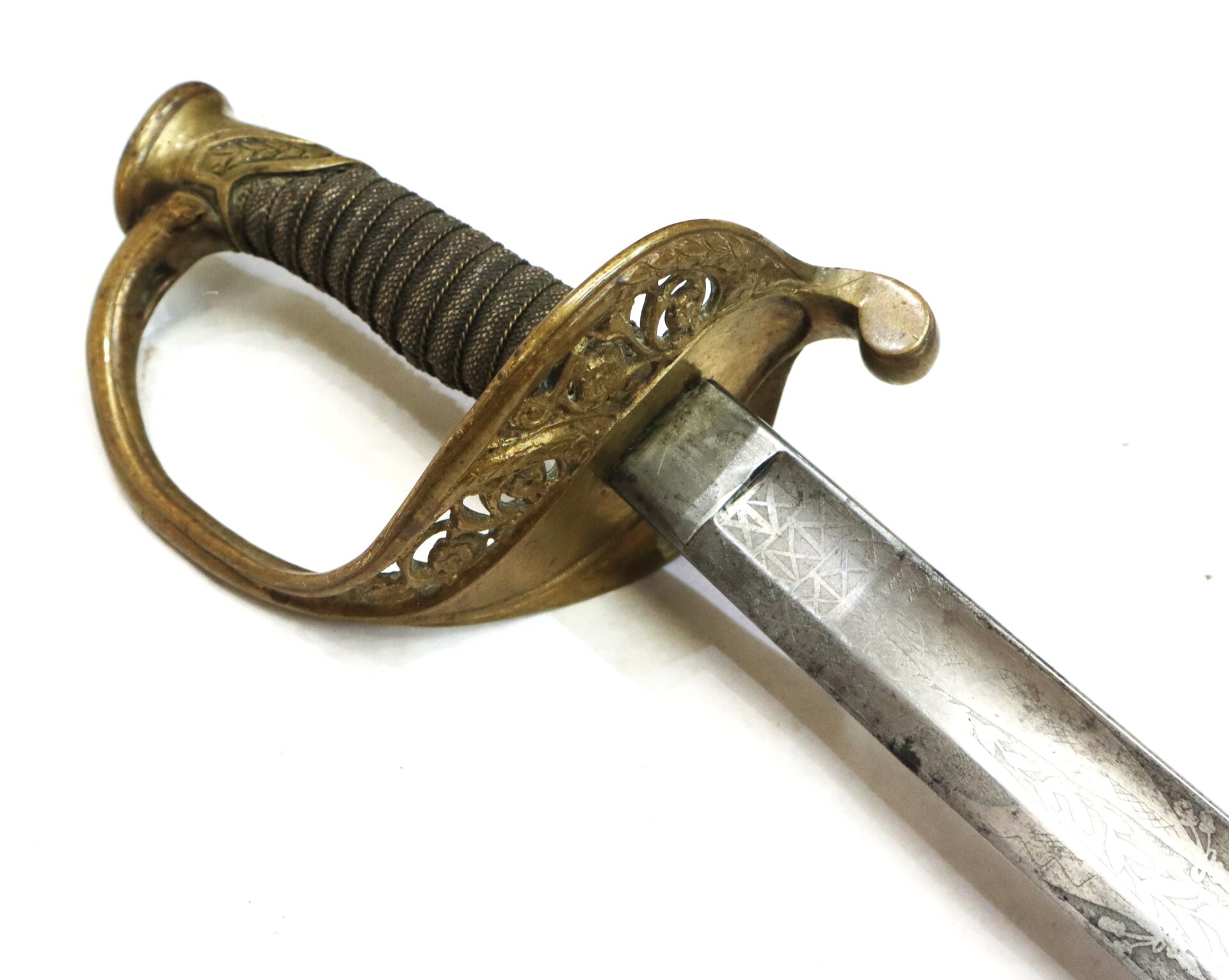 Close-up of an antique sword featuring a brass hilt with intricate designs and a partially visible engraved steel blade on a white background.