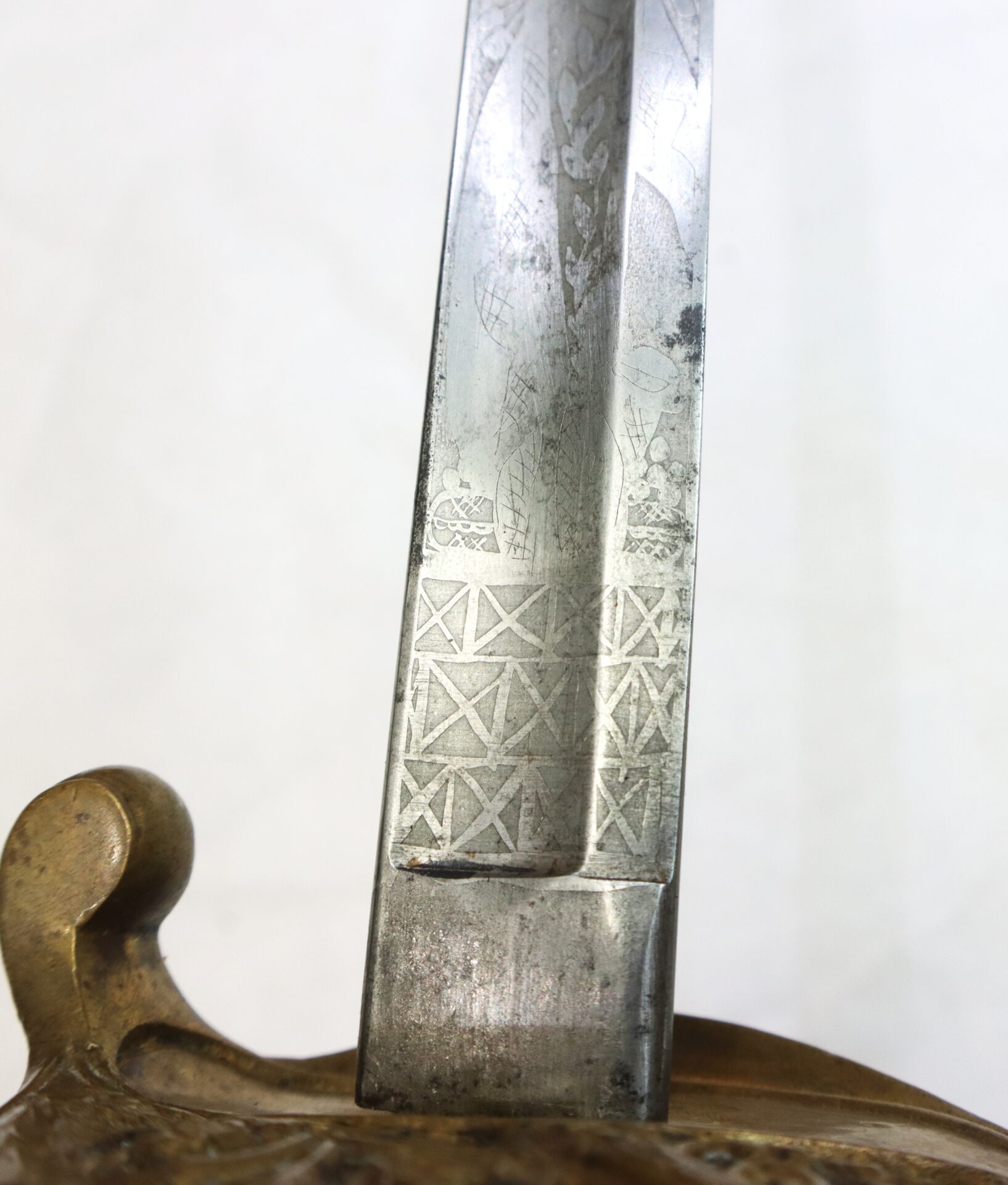 Close-up of a metal sword blade with engraved geometric and floral patterns near the hilt, partially sheathed in a decorative brass handle.