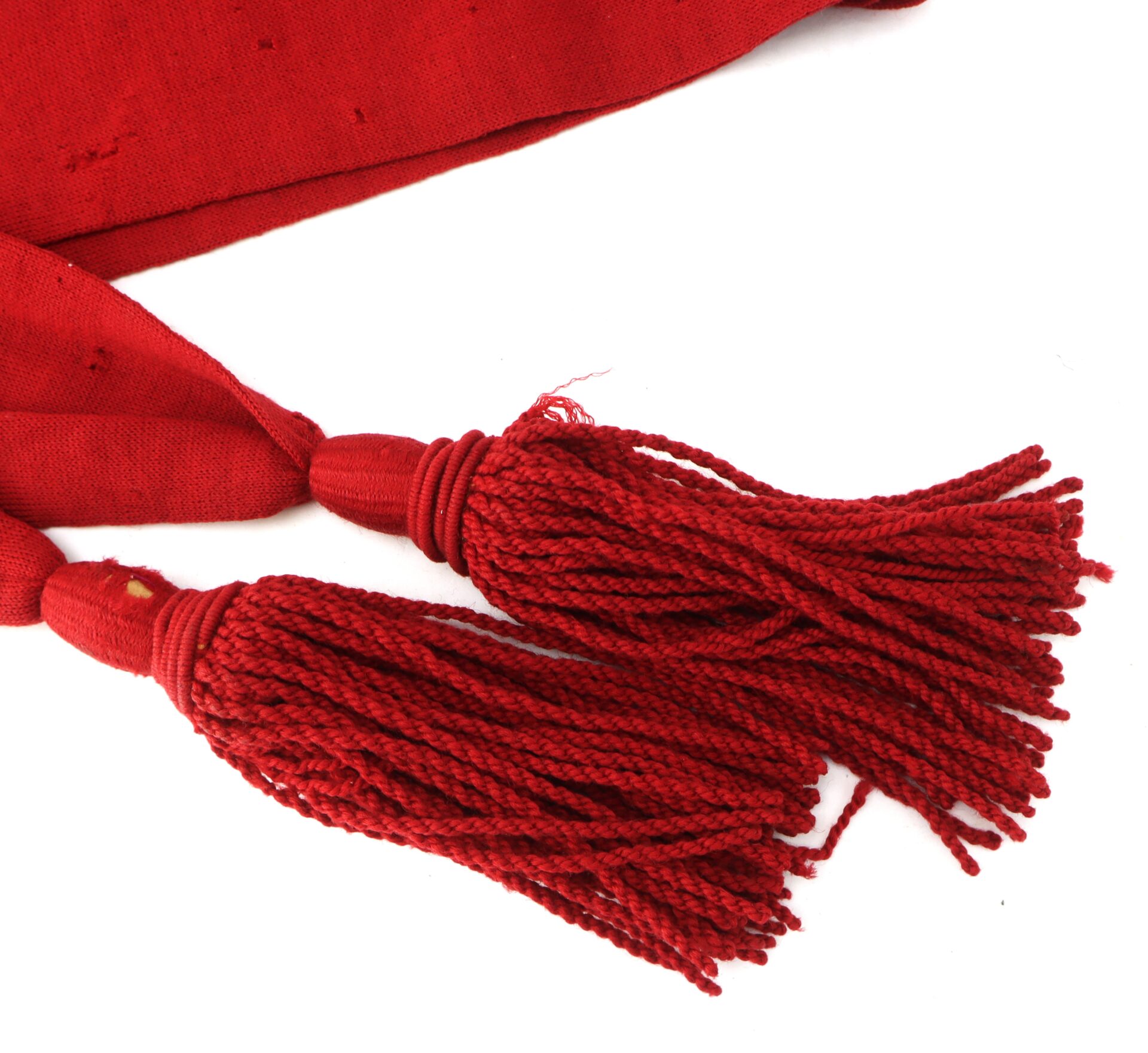 Two red tassels made of yarn are attached to a matching red fabric, lying flat on a white background.