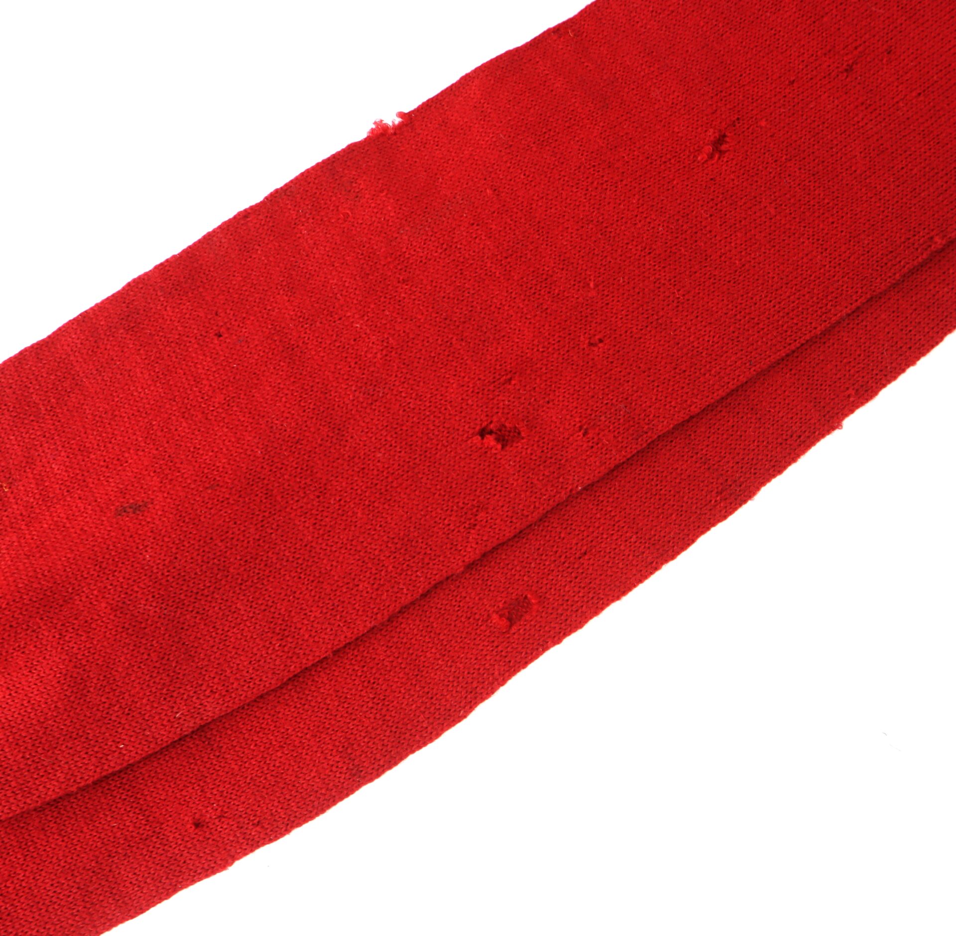 Close-up of a red fabric with visible small holes and signs of wear along the surface.