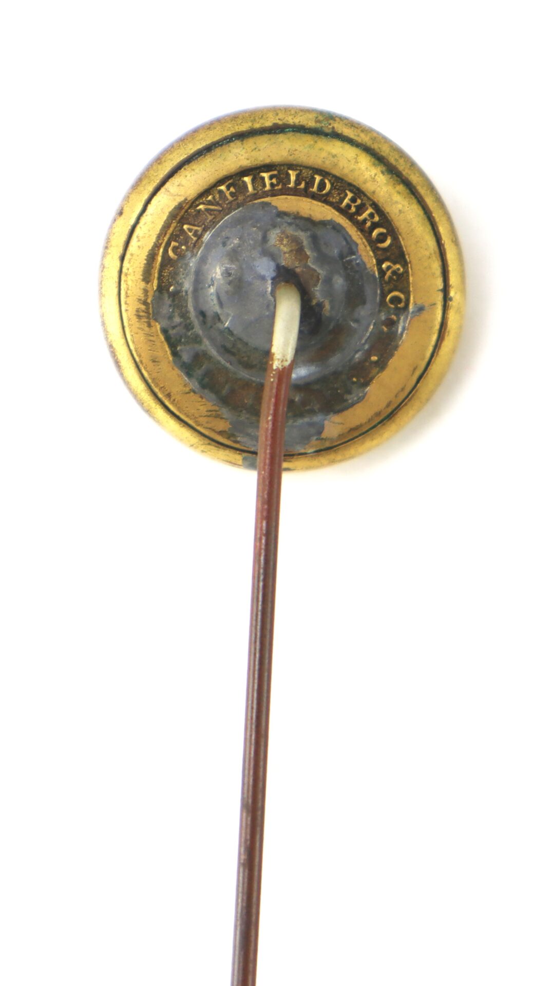 A close-up of the backside of a round gold stickpin with "CANFIELD BRO & CO" engraved on the back plate, set against a white background.