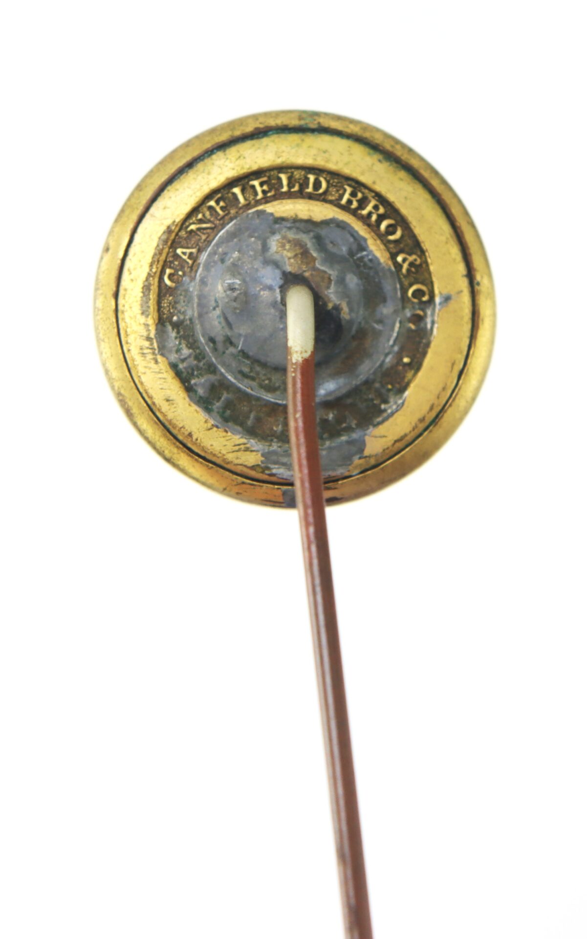 A close-up of the back of a gold stick pin with "CANFIELD BRO & CO" engraved around the rim, showing the pin inserted into the metal.