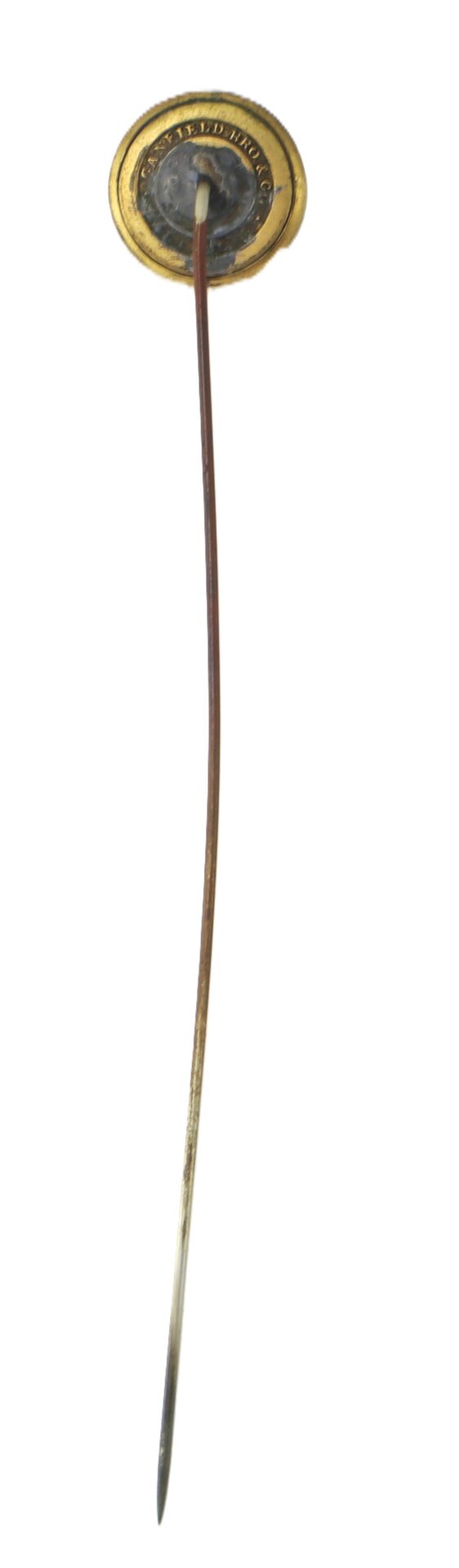 A vintage gold-colored stick pin with a circular decorative top and a long, thin metal shaft, photographed on a white background.