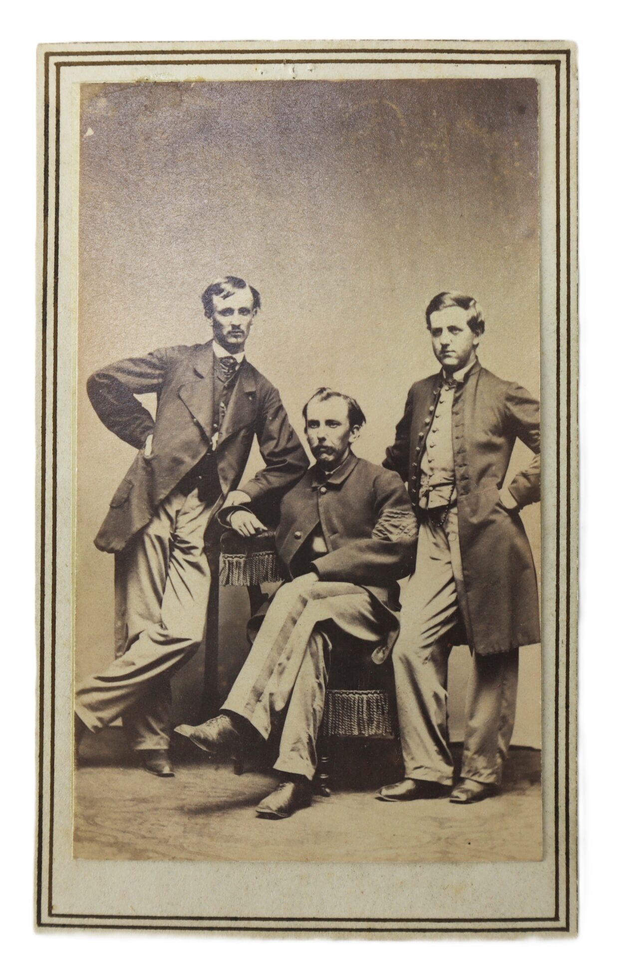 Three men in 19th-century formal attire pose for a studio portrait; one is seated while the other two stand on either side of him.
