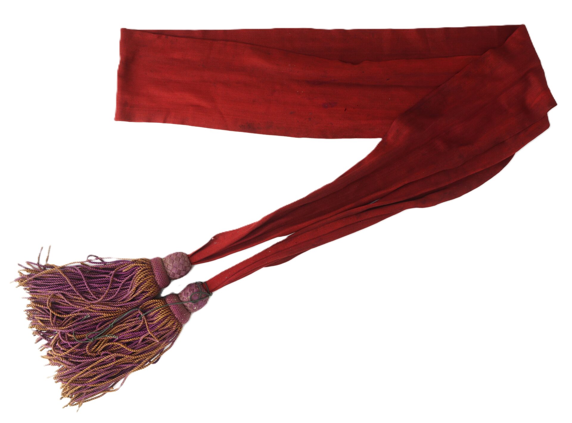 A long, red fabric sash with two decorative purple and gold tassels at the ends, laid out on a white background.