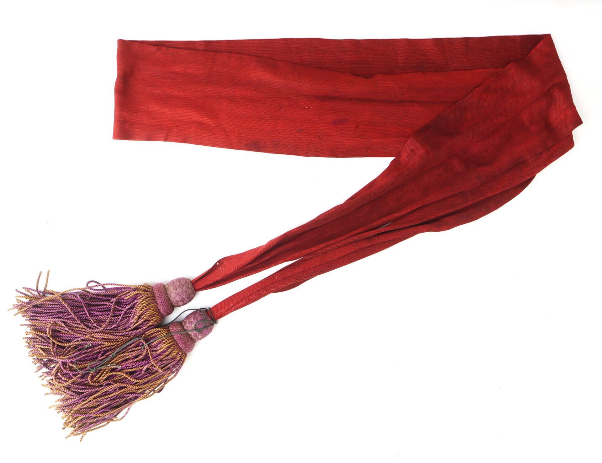 A long, red silk sash with two ends featuring pink and gold tassels, laid out flat on a white background.