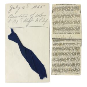 A handwritten note dated July 4, 1865, labeled "Presentation of colors" with a blue fabric strip attached, next to two yellowed newspaper clippings about the flag presentation.