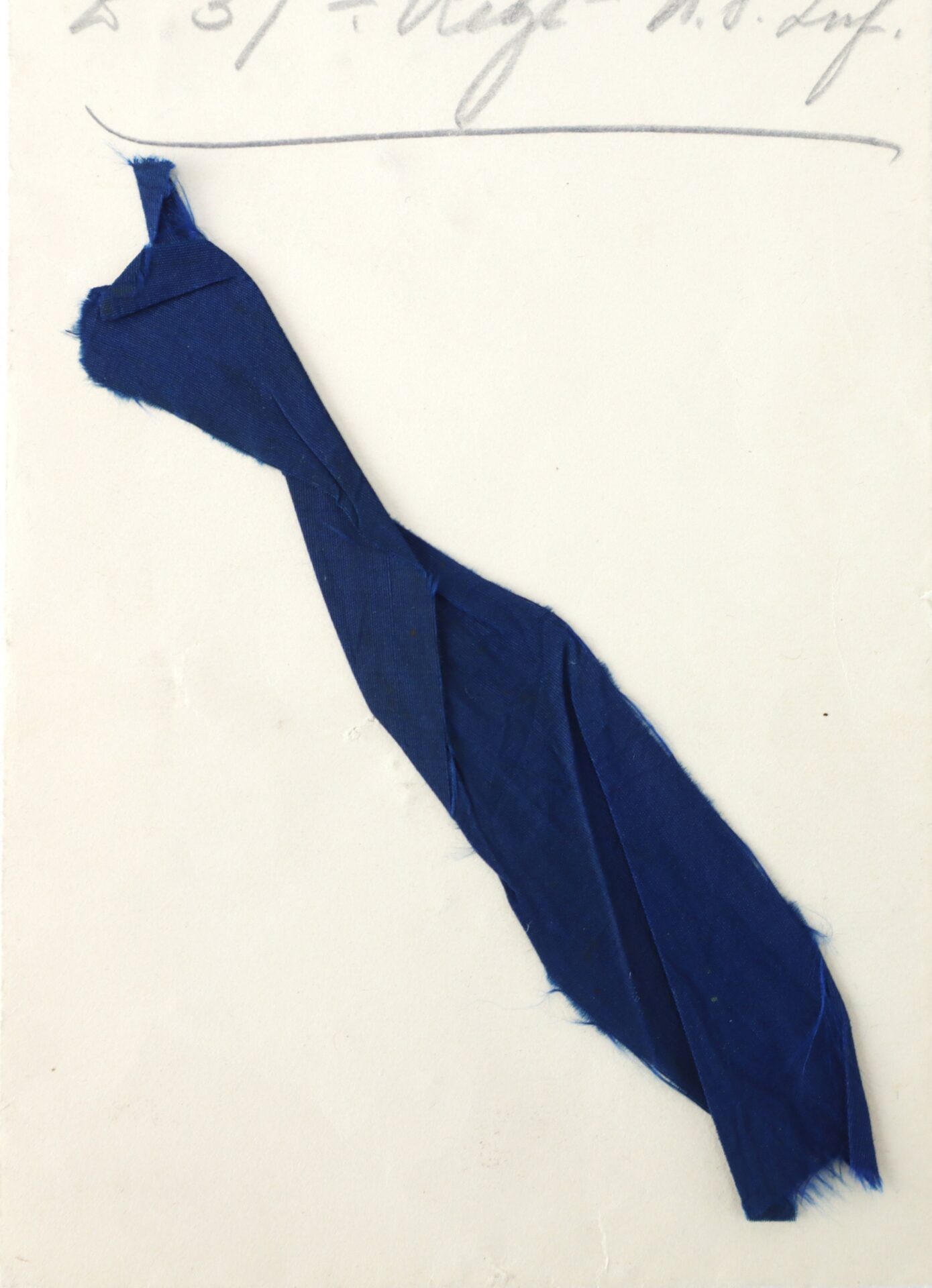 A twisted strip of dark blue fabric is attached to a white surface with handwritten text partially visible at the top.