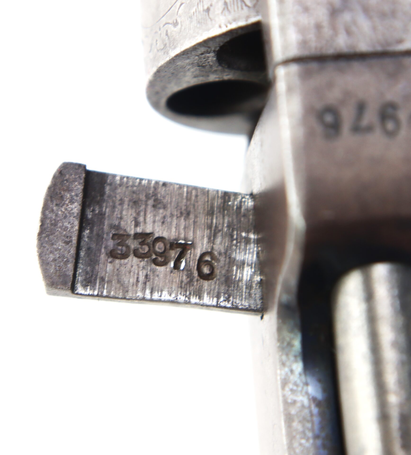 Close-up view of a metal firearm part with the serial number 33976 engraved on a protruding section.