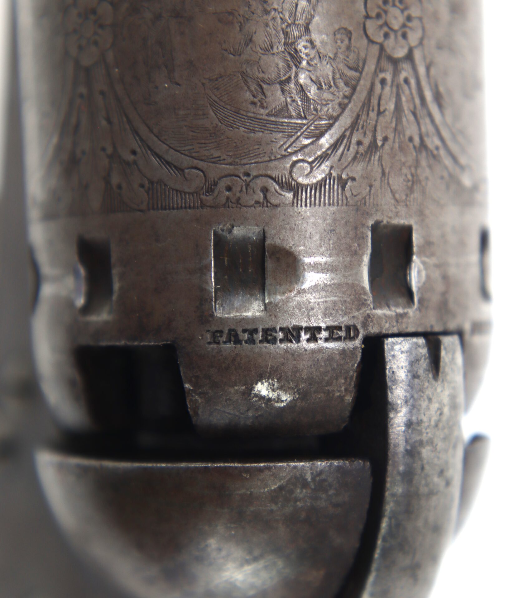 Close-up of an engraved metal surface on a firearm cylinder with the word "PATENTED" stamped below the notches.
