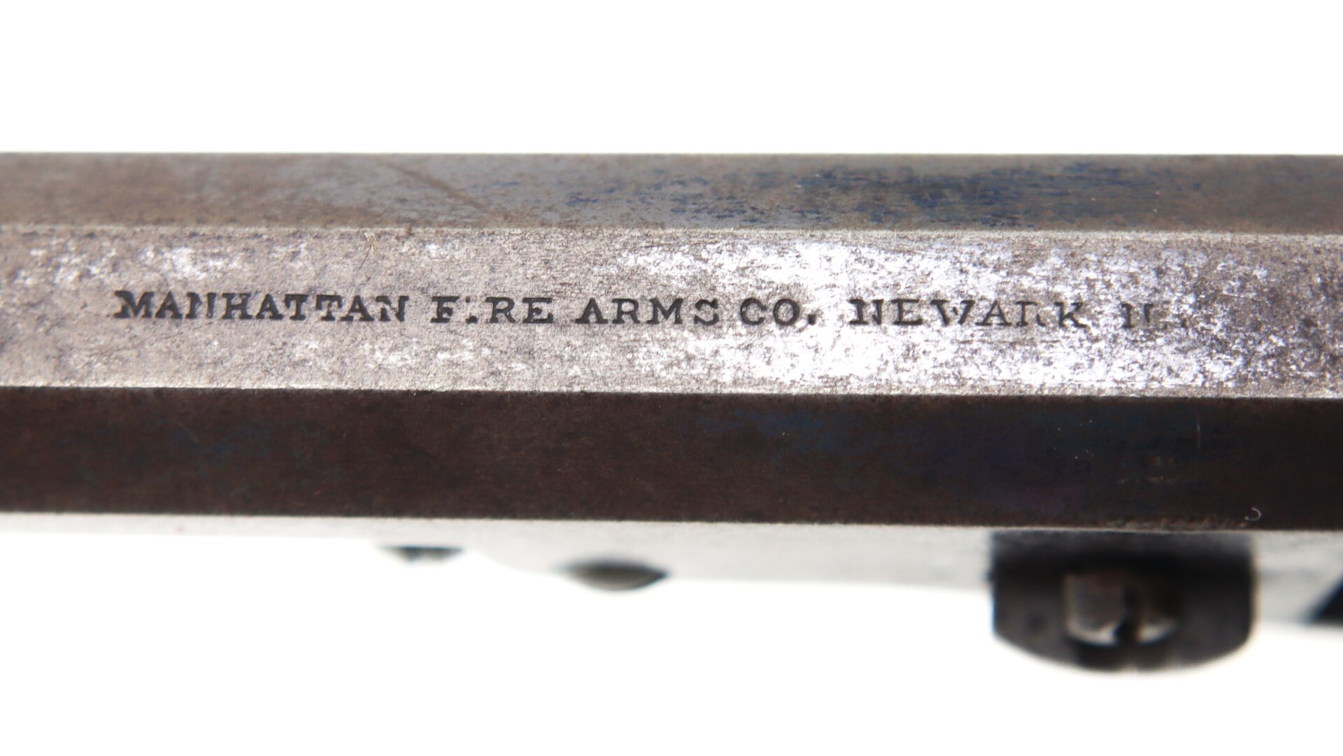 Close-up of metal surface with engraved text reading "MANHATTAN F. RE ARMS CO. NEWARK N.J.