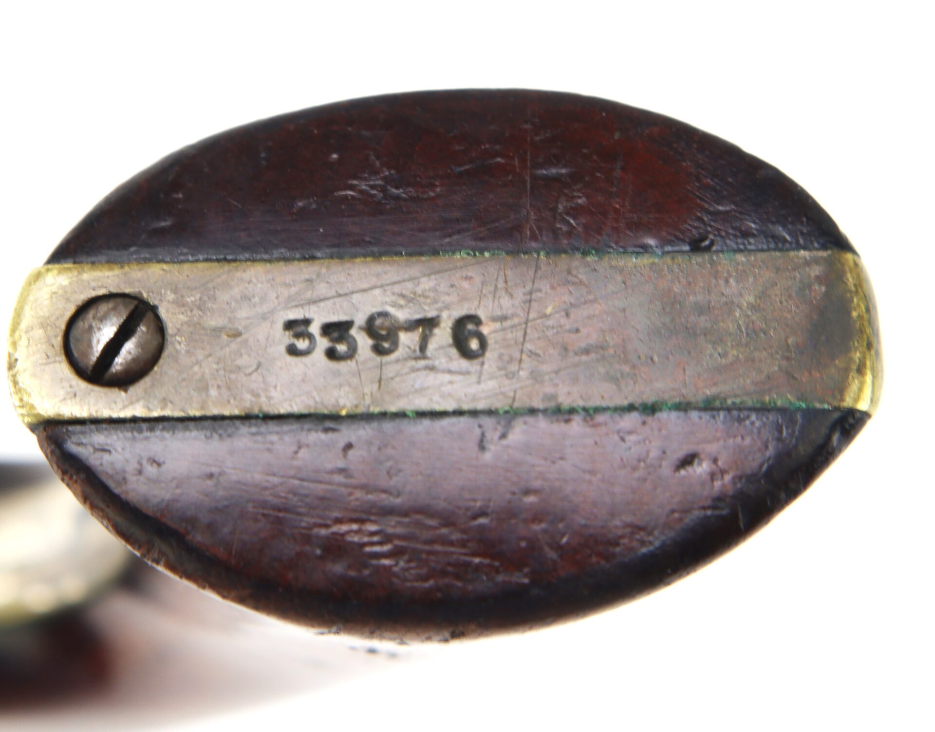 Close-up of a wooden object with a brass or metal strip attached by a screw, stamped with the number "53976.