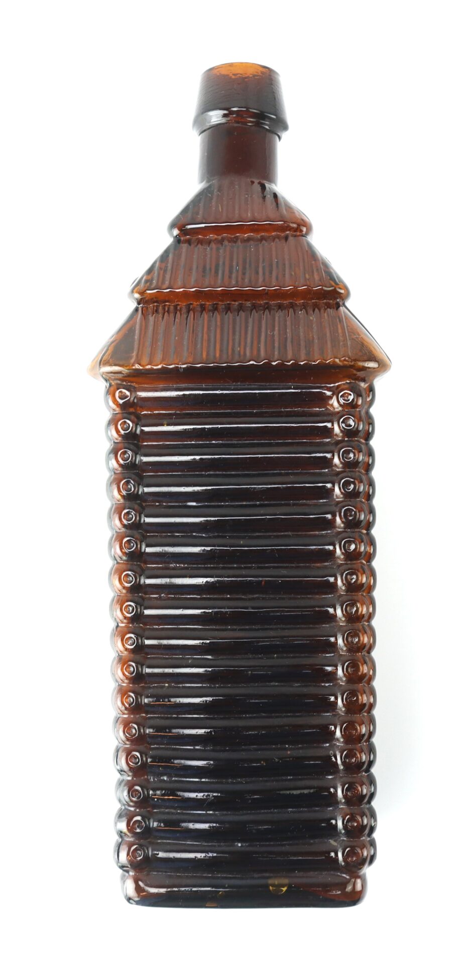 Tall, brown glass bottle shaped like a log cabin with textured sides and a ribbed roof-like top.